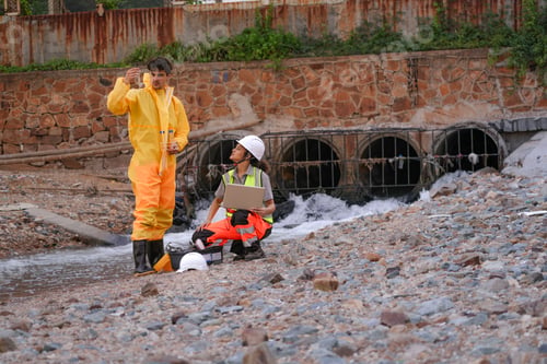 Preview: Environmental field team in protective gear analyzes water samples on a polluted beach. One holds a