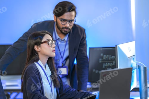 Preview: A focused male engineer in a navy blazer with an ID lanyard taking handwritten notes at the workstat