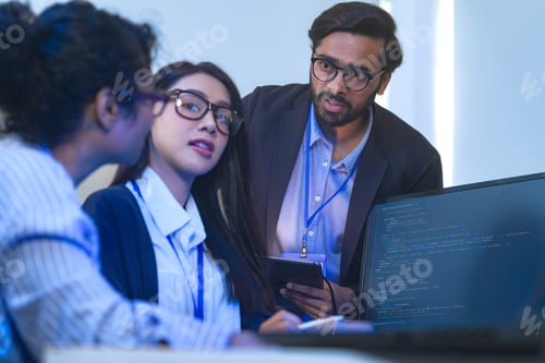 Preview: A bearded developer in a dark suit gesturing toward the code on the bright screen, at a glowing blue