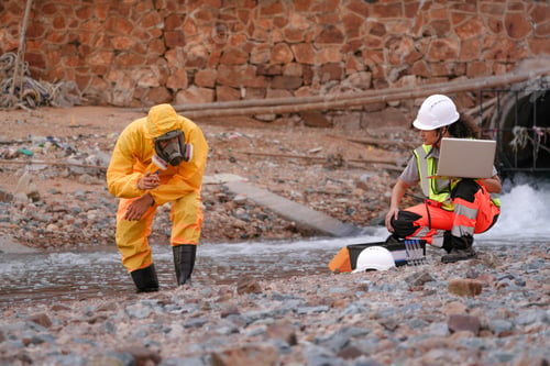 Preview: Environmental field team in protective gear analyzes water samples on a polluted beach. One holds a