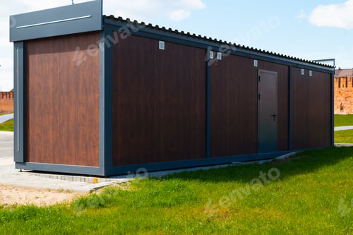 Preview: A modular building stands in an open field with grass surrounding it. The structure features a moder