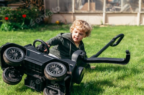 Preview: A young child is playing on green grass with a toy car that is flipped upside down. The child appear