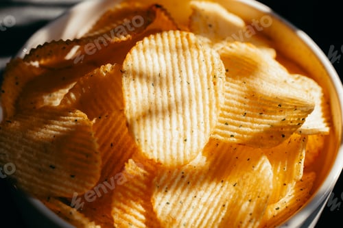 Preview: A bowl filled with crispy potato chips sits on a surface, capturing light and shadow. The chips disp