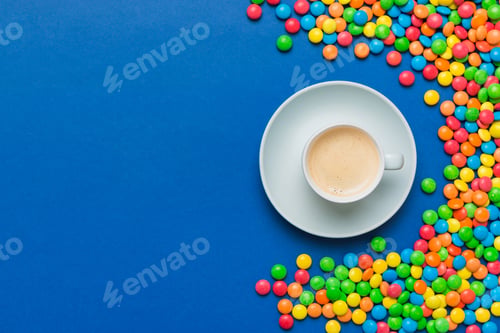 Preview: Coffee cup with chocolates and colored candy. Top view on table background with copy space