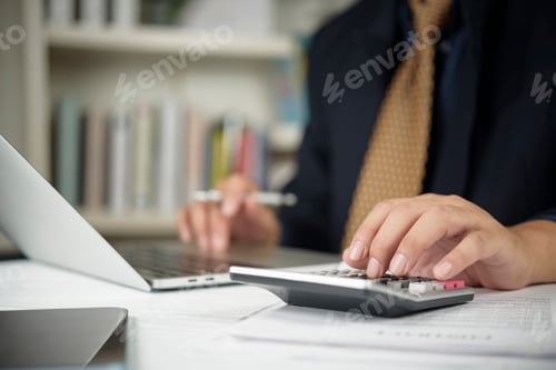 Preview: Close-up of an accountant's hands using a calculator to calculate tax or financial budget on a woode