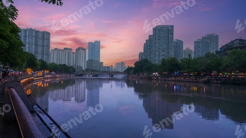 Preview: City skyline along a calm river during sunset in Chengdu, China. The purple and pink sky reflects on
