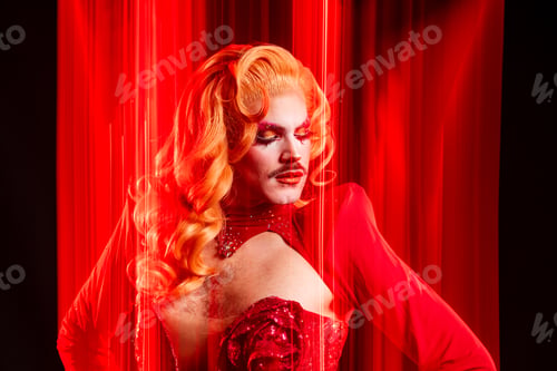 Preview: Drag Queen Poses in Red With Bright Light in Studio Setting During a Queer Event