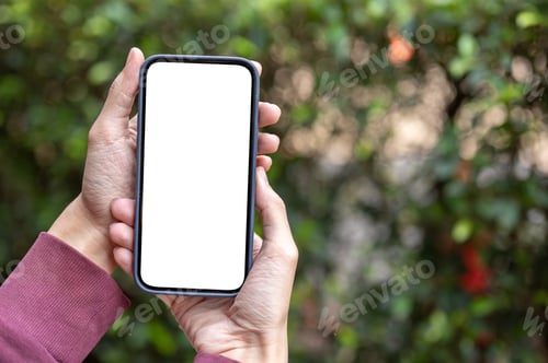 Preview: Close up of a man's hands holding white screen smartphone with blurred garden trees in background.