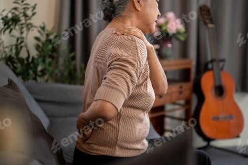Preview: Elderly old asian woman grandma holding back and shoulder getting pain ache while sitting on sofa.