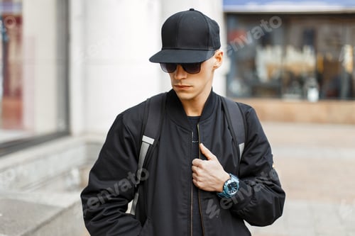 Preview: Handsome young man with sunglasses in a black jacket with a backpack in the city