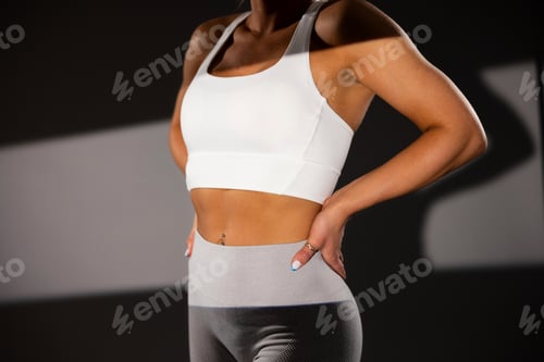 Preview: Fit woman in white sports bra and gray leggings standing confidently in gym setting