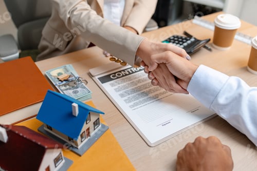 Preview: A real estate agent and a client are shaking hands after signing a house purchase agreement. The des