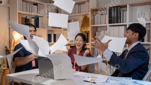 Preview: Business team celebrating success in office, throwing documents in the air with joy, expressing achi