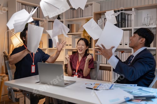 Preview: Business team celebrating success in office, throwing documents in the air with joy, expressing achi