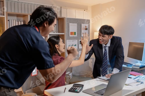 Preview: Business colleagues celebrating success in office, smiling and giving high five across desk, showing