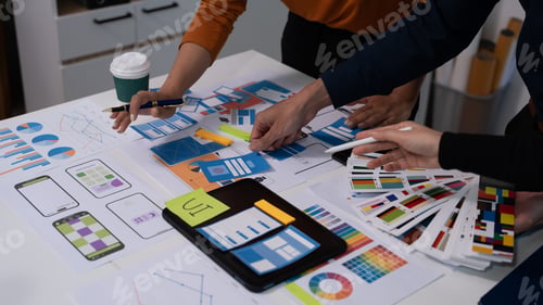 Preview: Team of coworkers reviewing printed design mockups and charts on a table in an office, collaborating