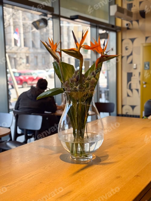 Preview: Bird of paradise flowers stand in a glass vase on a communal cafe table. Warm design, stillness, nat