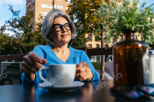 Preview: Senior woman relaxing outdoors, enjoying a coffee while looking up with a thoughtful smile