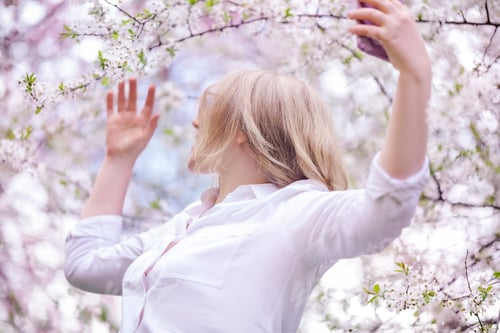 Preview: Inspired woman reaching for blooming tree flowers. Appreciation of nature beauty and spring spirit.