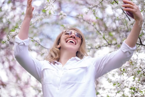 Preview: Cheerful woman in park raising arms to blooming branches. Joy and celebration of spring awakening.