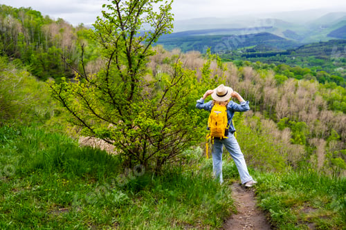 Preview: Carefree woman with yellow backpack standing on trail and looking at vast green mountain valley. Sum