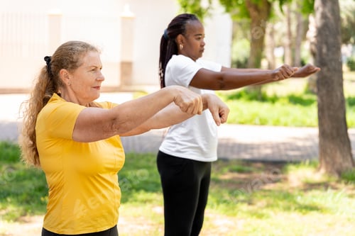 Preview: Diverse senior women friends stretching arms together in park, enjoying healthy active lifestyle