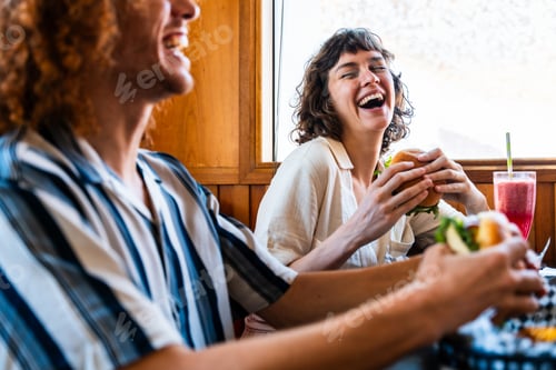 Preview: Friends laughing together eating burgers at diner