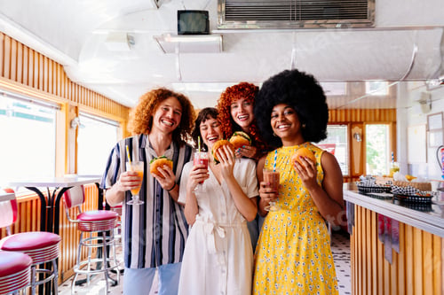 Preview: Young multiethnic friends enjoying food and drinks at vintage diner