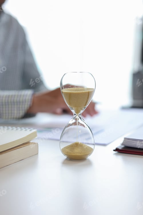 Preview: Businessman at a desk with an hourglass in the foreground, representing a time management concept.