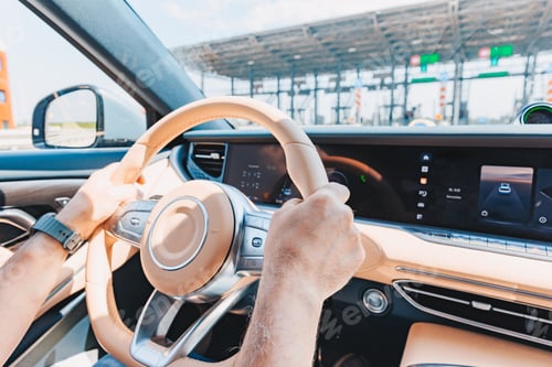 Preview: Steering a modern sedan with a beige interior at a toll booth under bright daylight