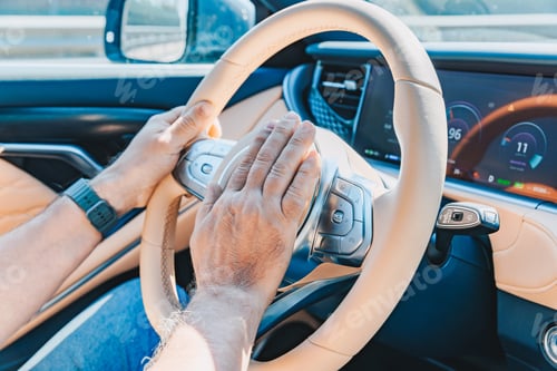 Preview: Hand pressing the horn on the steering wheel inside a luxury modern car during daytime