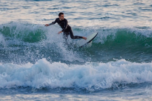 Preview: Surfer on surfboard riding ocean wave at evening light