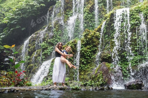 Preview: Happy mother and daughter hugging near waterfall in Bali