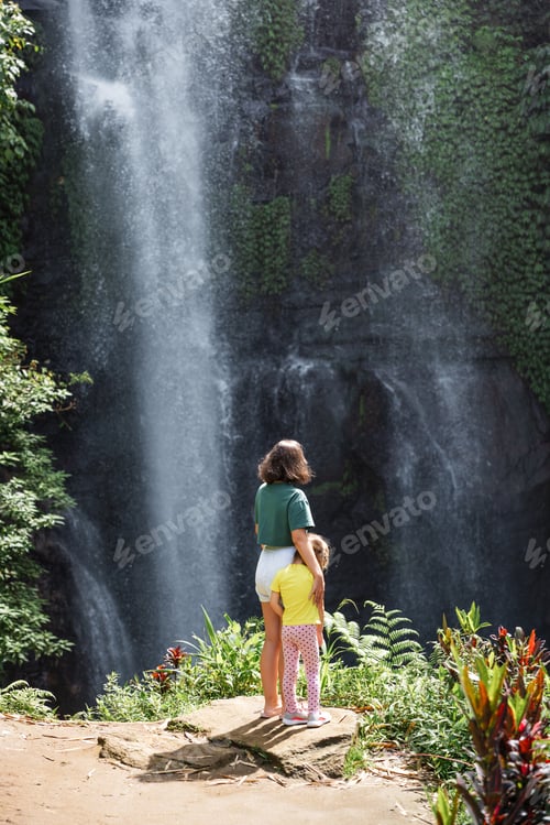 Preview: Mother and daughter admiring tropical waterfall in sunny day