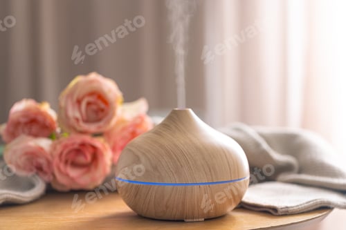 Preview: Wooden aroma diffuser releasing mist beside pink roses. Spa wellness aromatherapy.