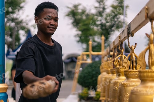 Preview: Young man ringing traditional golden bells at a temple for good fortune