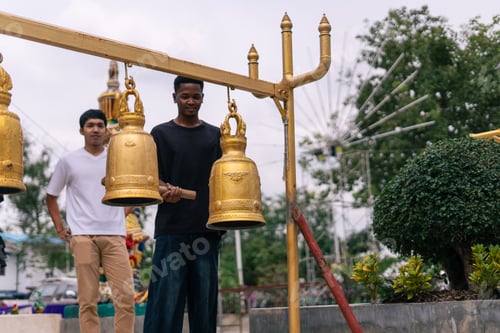 Preview: Young men ringing golden buddhist bells at temple, experiencing spiritual tradition
