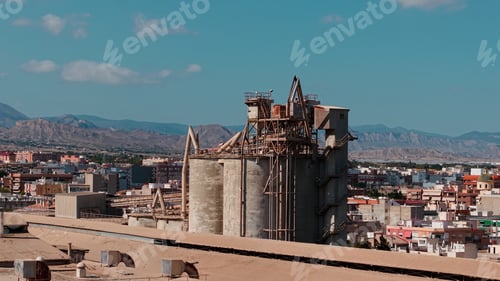 Preview: Industrial cement plant operating with large silos over urban landscape