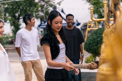 Preview: Young asian woman ringing golden temple bells, experiencing thai spirituality with friends