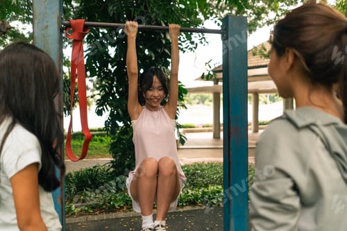 Preview: Young asian woman smiling while working out on outdoor pull up bar