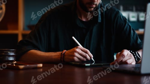 Preview: Creative Man Using Stylus Pen on Digital Tablet in Dimly Lit Workspace