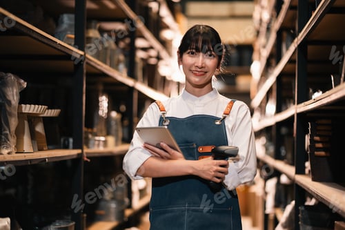 Preview: Young woman warehouse worker holding tablet and scanner in aisle