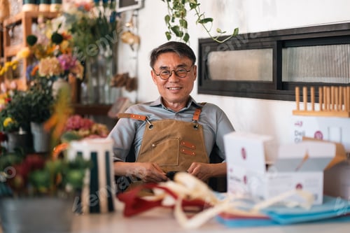 Preview: Smiling florist in apron at flower shop counter