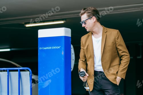 Preview: Electric vehicle charging station in parking garage, man with charging cable