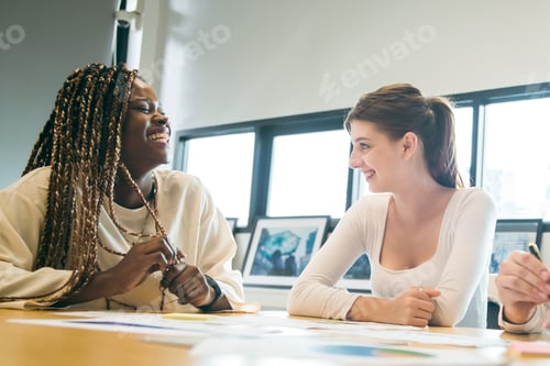 Preview: Diverse woman smiling in office meeting with coworker, friendly teamwork scene