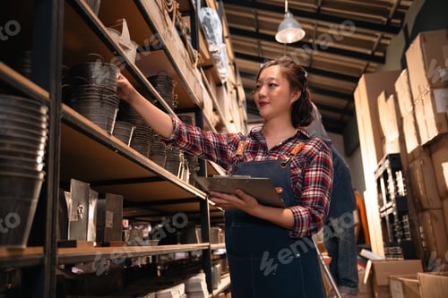 Preview: Young woman in warehouse shelf with clipboard and bucket