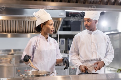 Preview: Chefs in professional kitchen collaborating during cooking process, wearing white uniforms and discu