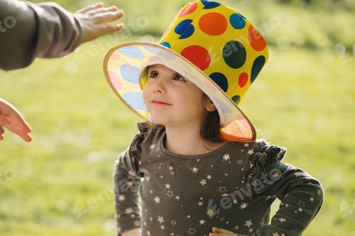 Preview: Vertical portrait of beautiful little girl playing in clown hat in park.
