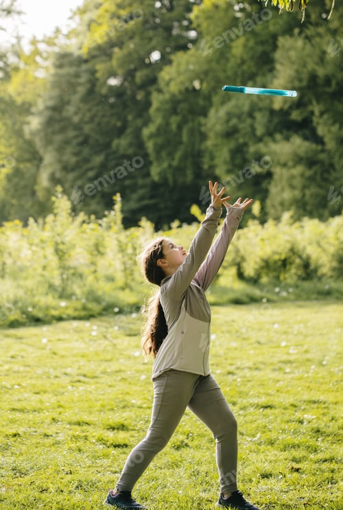 Preview: A full-length vertical portrait of a girl playing with a thrown object in a park.