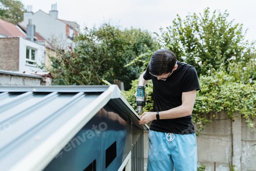 Preview: A young brunette man installs a roof on a metal shed with a screwdriver.
